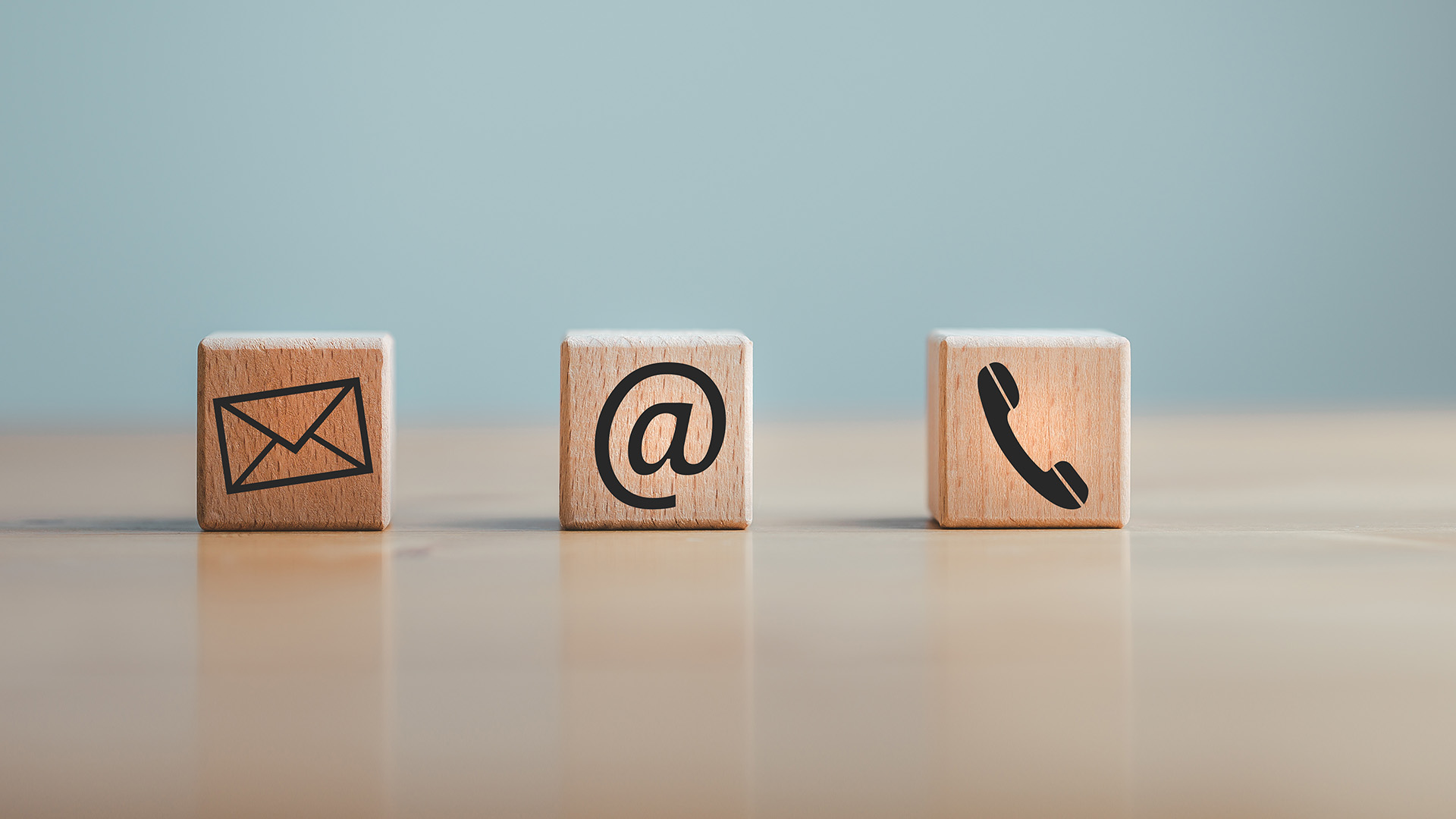 The image shows four wooden blocks arranged on a surface, each bearing a different symbol  an envelope, a phone, an email icon, and a house.