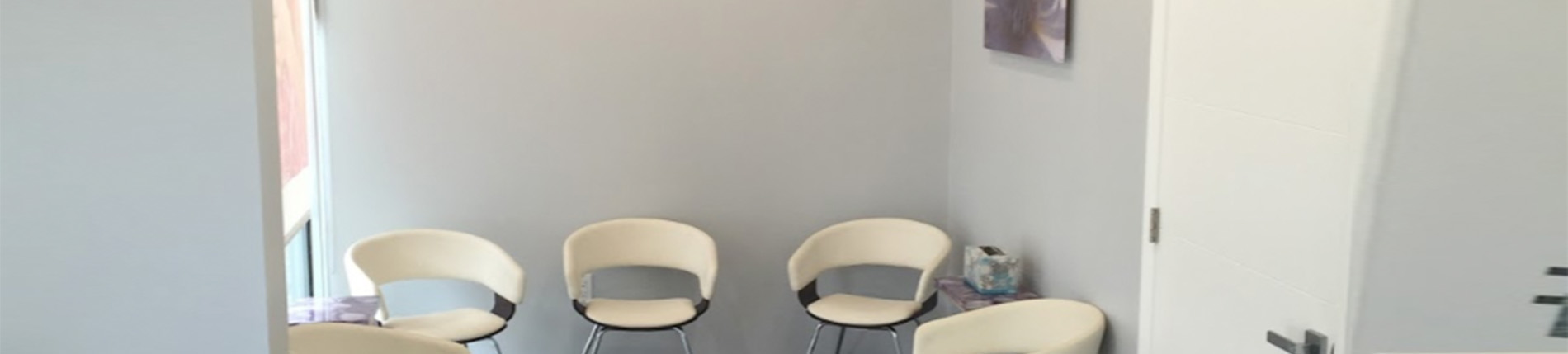 The image shows an interior space with a white wall, two chairs, and a table set up against the wall.