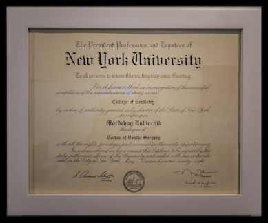 The image shows a framed diploma from New York University with a focus on academic achievement, featuring text, seals, and signatures, displayed against a wall.