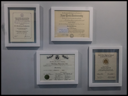 The image displays a collection of framed documents, including what appears to be diplomas, certificates, and possibly awards, arranged on a wall with a light background.