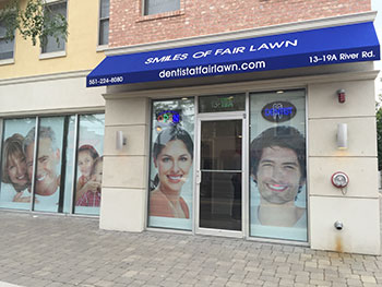 The image shows a storefront with a blue awning featuring a large advertisement for dental services, including a photo of smiling people, and text indicating  SMILES OF FAIR LAWN  and a phone number.