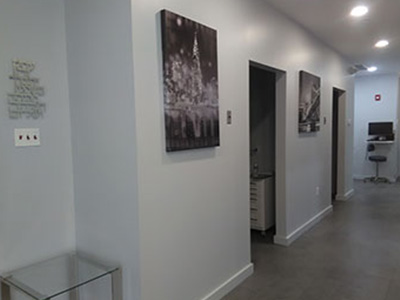 The image depicts an interior hallway of a building with walls painted in light gray, dark gray baseboards, and white trim. There are framed photographs hanging on the wall, and a glass display case is visible at the end of the hall. The flooring appears to be a dark-colored tile or stone, and there are no people present in the scene.