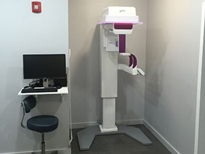 The image shows a modern dental chair with a computerized system, likely for digital X-rays or imaging, situated within a clean, professional office space.