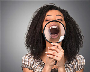 The image features a woman with her mouth open wide, holding a magnifying glass up to her face, seemingly in an exaggerated expression of surprise or shock.