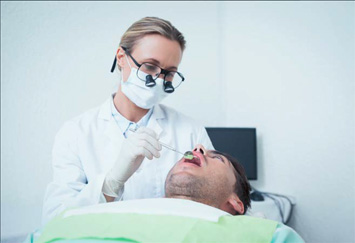 The image shows a person receiving medical attention from another individual who appears to be a healthcare professional, with both individuals wearing masks and gloves, suggesting a clinical setting.