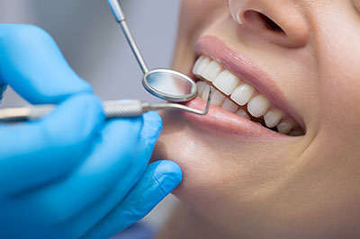 The image shows a dental professional performing oral care on a patient, with the patient s mouth open wide for treatment, wearing protective gloves, and using specialized dental tools.