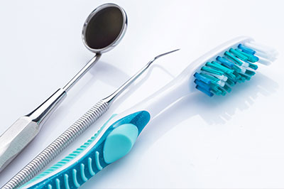 The image shows a collection of dental tools including a toothbrush with blue bristles, a pair of tweezers, and a metal dental instrument on a white background.