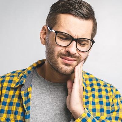The image depicts a man with glasses, who appears to be in pain or discomfort, holding his jaw while wearing a plaid shirt.