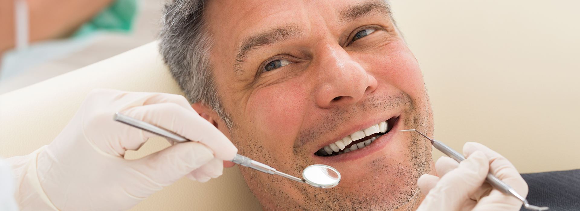 A man with a toothy smile receiving dental care in a chair, surrounded by dental tools and equipment, including a dentist s hand holding a drill.