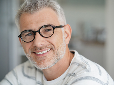 The image shows a man with short hair, wearing glasses and a white shirt, smiling at the camera.