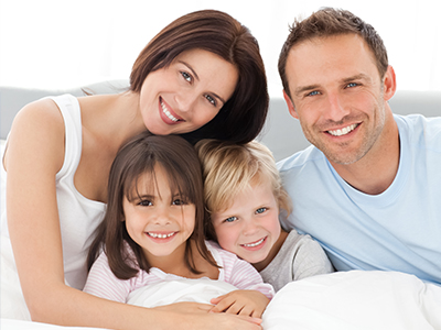 A family of four posing together on a bed with two adults and two children, smiling at the camera.